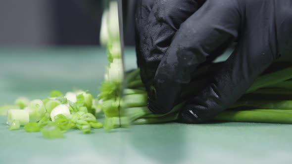 Cook's Hands in Black Gloves Slicing Green Onions Close Up