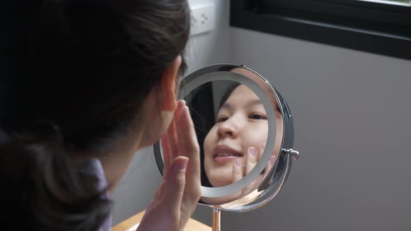 Reflection of Asian woman checking facial skin condtion
