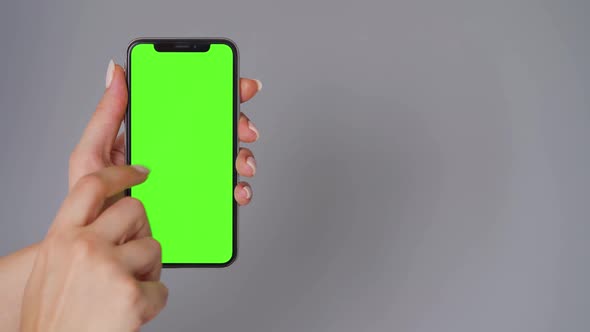 Female Hands Using a Smartphone with a Green Screen on a Gray Background. Chroma Key.