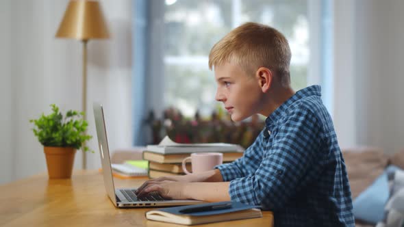 Portrait of Teenage Caucasian Boy Using Laptop While Studying at Home,