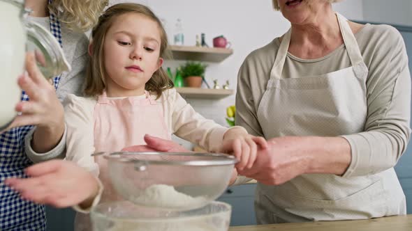 Handheld video of girl with mother and grandmother sifting flour. Shot with RED helium camera in 8K.