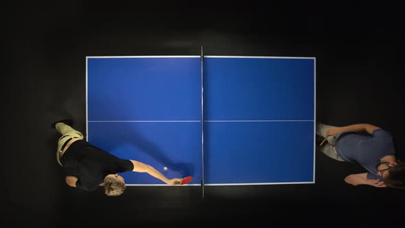 Two Young Men Playing Ping Pong Game Enjoying Competitive Sport in Dark Background. Top View