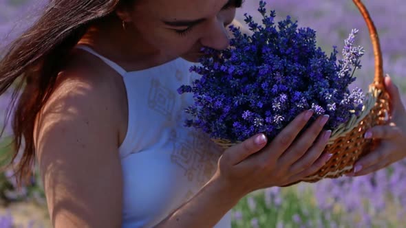 A young woman in a hat and white dress holds a wicker basket with lavender flowers.