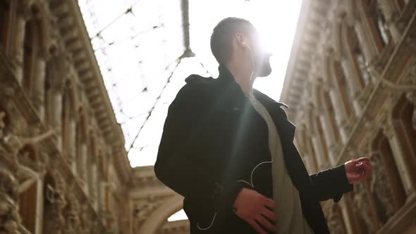 Young Caucasian Male in Heaphones Dancing Jumping Playing Imaginary Guitar in Beautiful Passageway