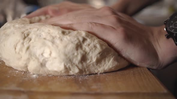 Baker's Hands Pressing And Kneading Dough On The Wooden Board - close up