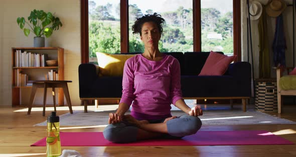 Mixed race woman practicing yoga and meditating while sitting on yoga mat at home