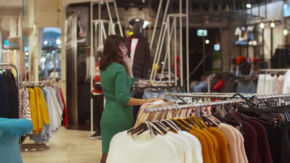 Woman in Dress Chooses Clothes and Talks on the Phone