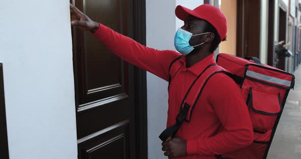 Young african man with thermal backpack rings the doorbell while wearing safety face mask