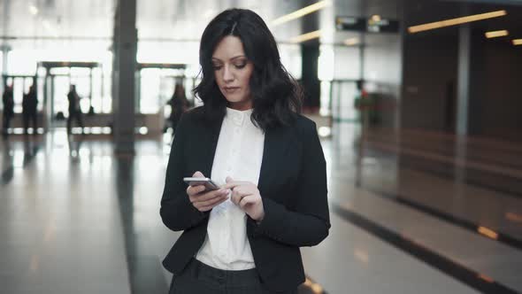 Young Business Woman Uses a Smartphone While Standing in the Lobby
