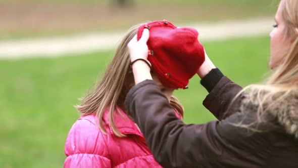 Mom putting cap on daughter's head and kissing her in forehead