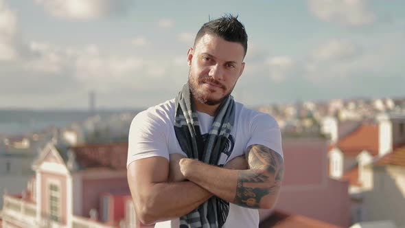 Smiling Young Man with Crossed Arms Standing on Rooftop.