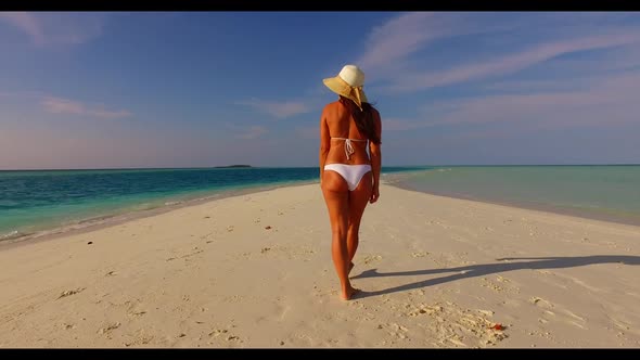 Female model tanning on idyllic coastline beach trip by shallow ocean with bright sand background of