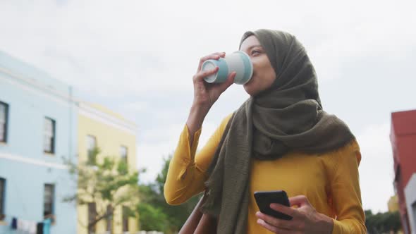 Woman wearing hijab using a phone and drinking a take away coffee