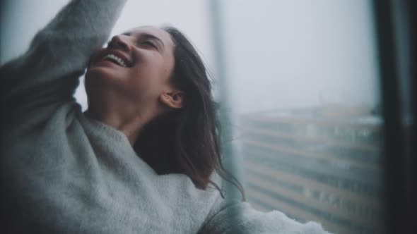 Woman stands outside a window with her hair blowing in the wind