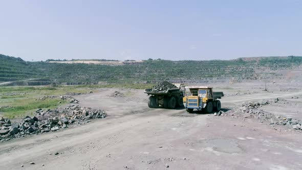 Mining Dump Trucks in Large Granite Open Pit Mine. Loaded Truck Rides on Road Quarry Ledge