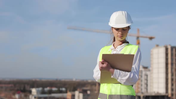 Portrait of Young Woman Engineer Who is Making Entries in Documents