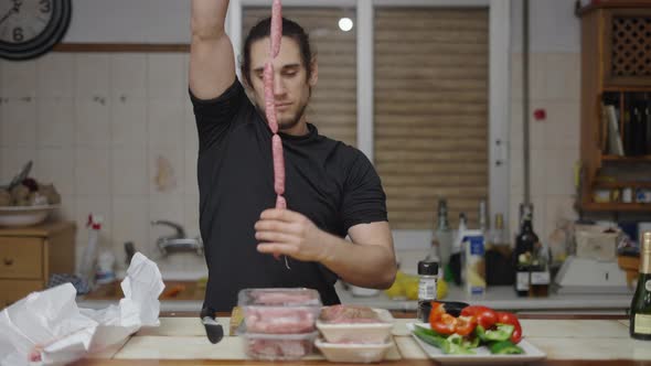 Goofy Young Adult Having Fun Playing with Raw Sausages in Traditional Spanish Kitchen