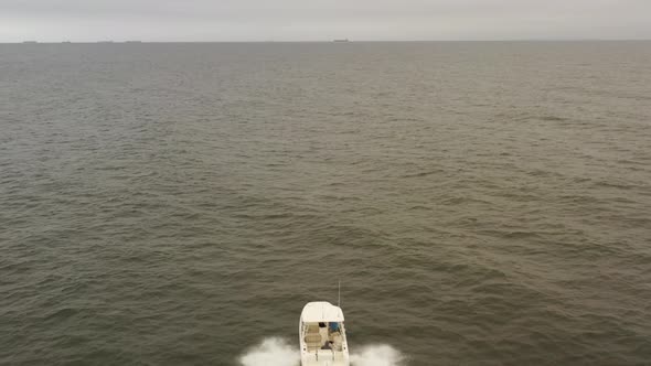 An aerial view of a small, white fishing boat speeding in the deep, green Atlantic Ocean by Long Isl