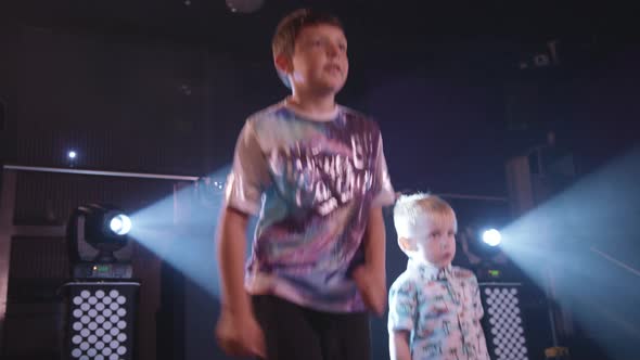 Two Young Boys Dance and Party at a Children's Disco with Bright White Lights Behind Them