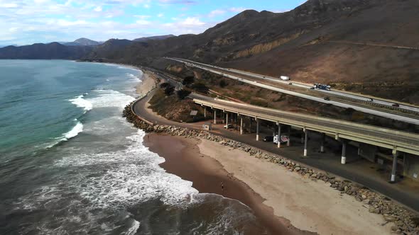 Aerial drone shot over a concrete bridge on the beach in Ventura next to the blue ocean waves and ca