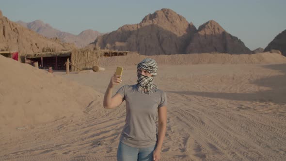 Tourist in Checkered Keffiyeh Trying to Find Mobile Network Using Cell Phone Standing in Desert