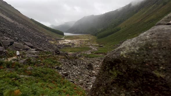 Reveal shot of hiker mountaineering in rocky mountains if Ireland during cloudy and rainy day - Pan