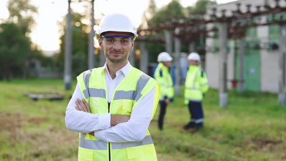 Male Engineer Technologist Standing Among High Voltage Electrical Lines With Her Arms Crossed