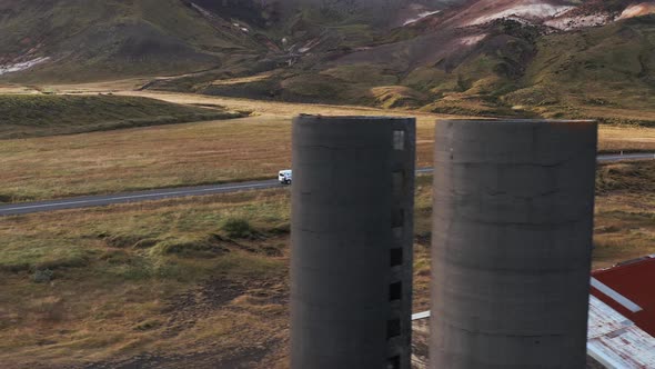 Abandoned broken building with grain silos in Icelandic valley, white car passing by in background,