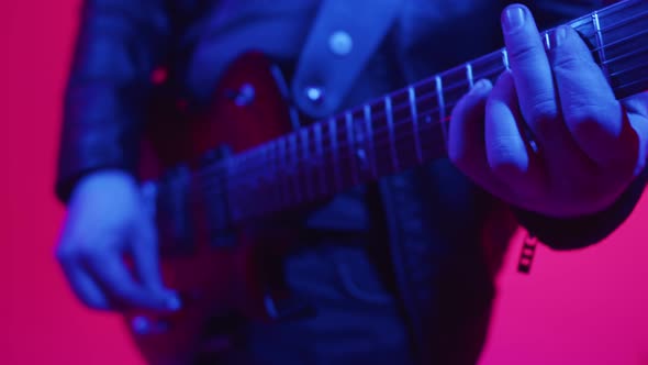 Male Musician Plays Electric Guitar Strings in Studio with Neon Lighting Closeup Hands