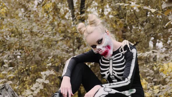 A girl with a scary make-up in a skeleton costume, a mask with rhinestones in a gloomy autumn forest