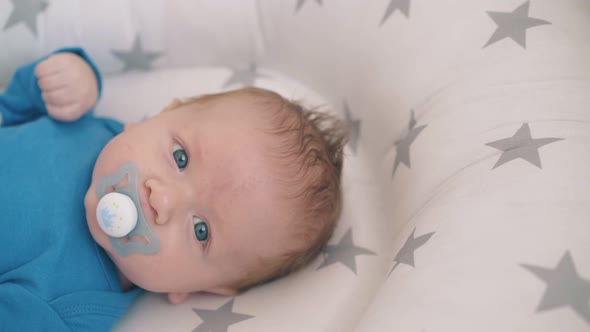 Cute Boy with Large Blue Eyes Sucks Pacifier in Soft Cocoon