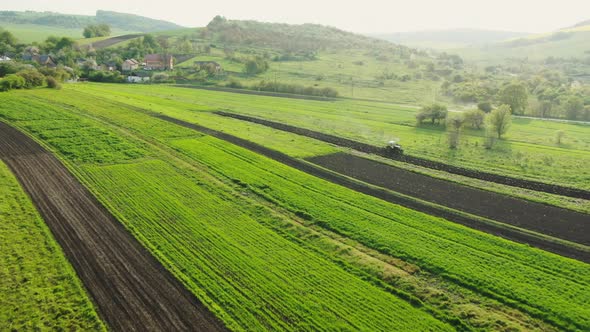 Drone Flight Over Green Spring Crops Growing in Agricultural Fields with a Tractor