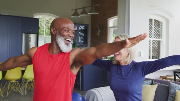 Mixed race senior couple performing stretching exercise together at home
