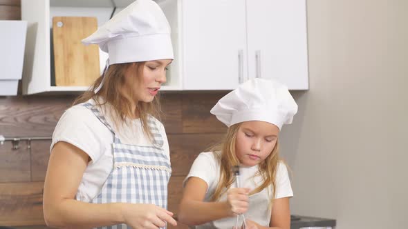 Young Mother and Her Daughter Prepare Dough in Kitchen