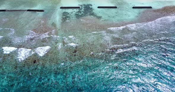 Daytime flying tourism shot of a white sandy paradise beach and turquoise sea background in vibrant 