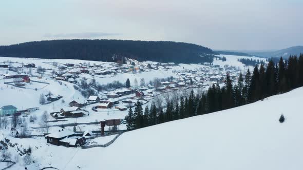 Aerial View of a Village with Wooden Houses on the Bank of a Frozen River in Winter