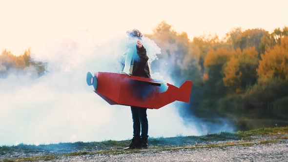 Happy Little Aviator Girl Standing Near Lake in Cardboard Plane Costume with Blue Color Smoke