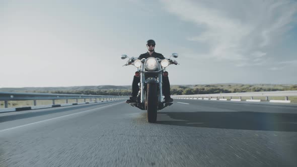 Biker in black glasses and helmet rides custom motorcycle on highway in steppe background sky