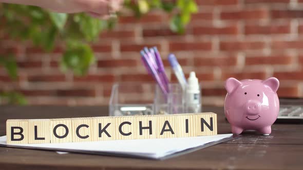 Inscription on the blocks the blockchain , hand of person puts money in the piggy bank.