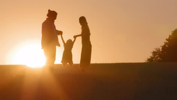 Family Silhouettes Parents with Child Plays Dad and Mom on Field in Sunset Light Flying in Air