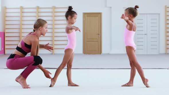 Female Gymnastic Trainer Putting Her Little Girl Student in the Right Position on Training in Sports