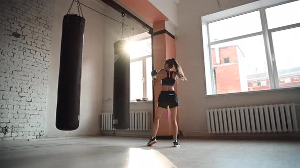 A Girl in Sports Clothes Is Engaged in Boxing and Works Out a Punch with Her Hand on a Punching Bag