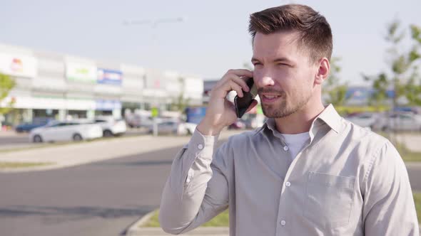 A Young Caucasian Man Talks on a Smartphone in an Urban Area