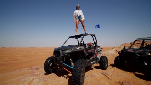 Young Woman Standing on the Roof of an Offroad Sand Buggy in the Desert