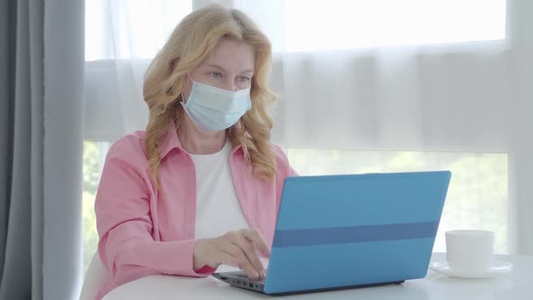 Mid-adult Caucasian Businesswoman in Face Mask Typing on Laptop Keyboard on Lockdown