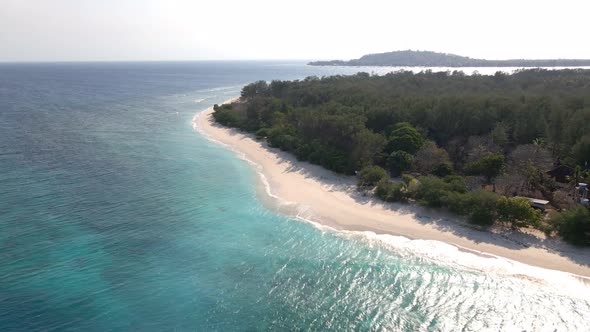 Descending aerial shot of crashing waves on sea shore of Gili Meno island.Epic travel paradise.