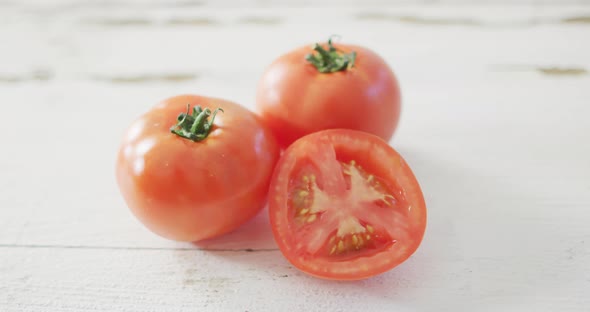 Video of halved and whole fresh red tomatoes on white rustic background