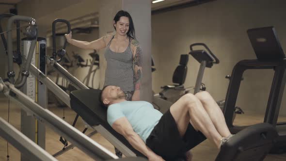 Smiling Female Trainer Looking After Man Doing Gravity Exercises. Young Concentrated Sportsman