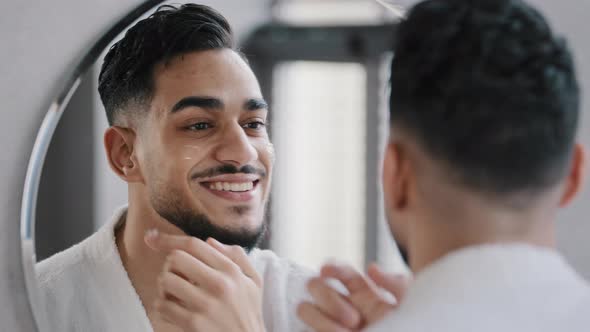 Arabian Indian Arab Hispanic Millennial 30s Bearded Man Applying Moisturizer Cream on Face Skin