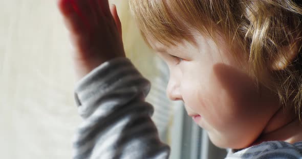 Close Up of Face of Happy Baby Looking Out of the Window and Running His Hand Over the Window Pane